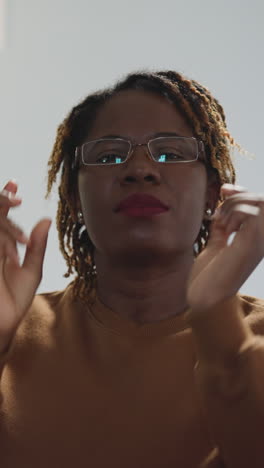 african american woman puts on glasses looking in camera and smiling. portrait of cheerful female person with dyed kinky hair against bright lamp closeup