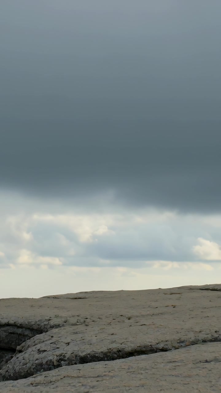 Vertical video: Advancing dark cloud bank moving over cracked rock ledge on coast, signaling storm