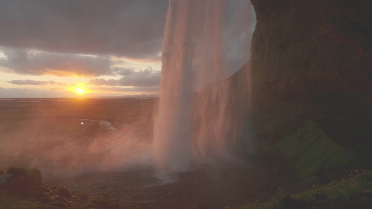 Cảnh quay điện ảnh 4K chuyển động chậm được quay từ phía sau thác Seljalandsfoss ở Nam Iceland lúc hoàng hôn. Ánh sáng vàng chiếu sáng thác nước đổ trong khi sương mù trôi lãng đãng khắp phong cảnh.