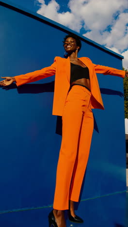 stylish woman in vibrant orange pantsuit against blue wall