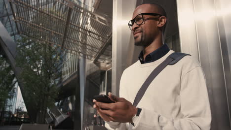 african american businessman walking through city using smart phone