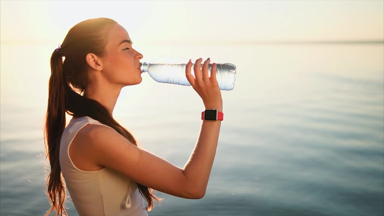 Woman drinking water by the sea at sunrise