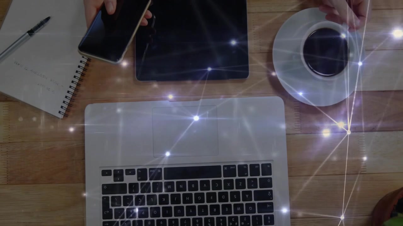 ノートパソコンのキーボード、タブレット、スマートフォン、コーヒー、そして光るネットワークオーバーレイが映し出されたワークスペースのレイアウト。