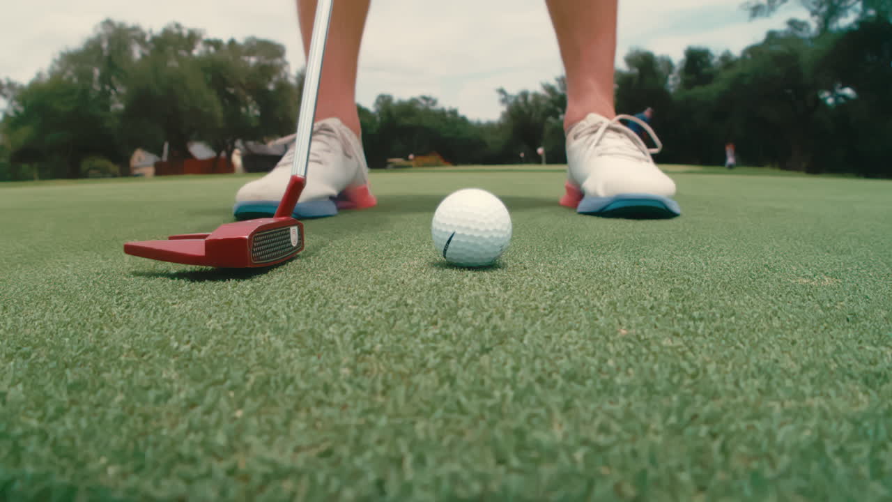 Extreme slow-motion close-up of golfer’s feet and putter taking back and striking ball. Highlights precision, stance, technique, and short game control