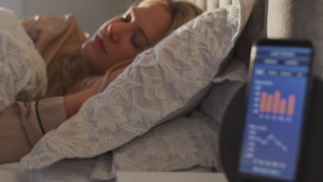 woman sleeping in bed with sleep data app running on mobile phone on bedside