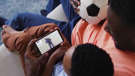 Composite-of-father-and-son-at-home-watching-judo-match-on-smartphone