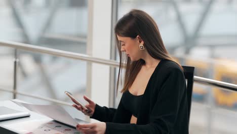 Pretty-girl-in-a-business-suit-working-at-the-table-receives-a-joyful-message-on-a-smartphone