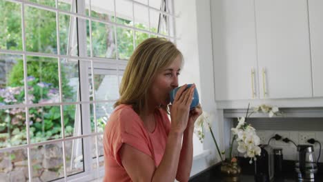 caucasian senior woman standing in kitchen at home drinking cup of coffee