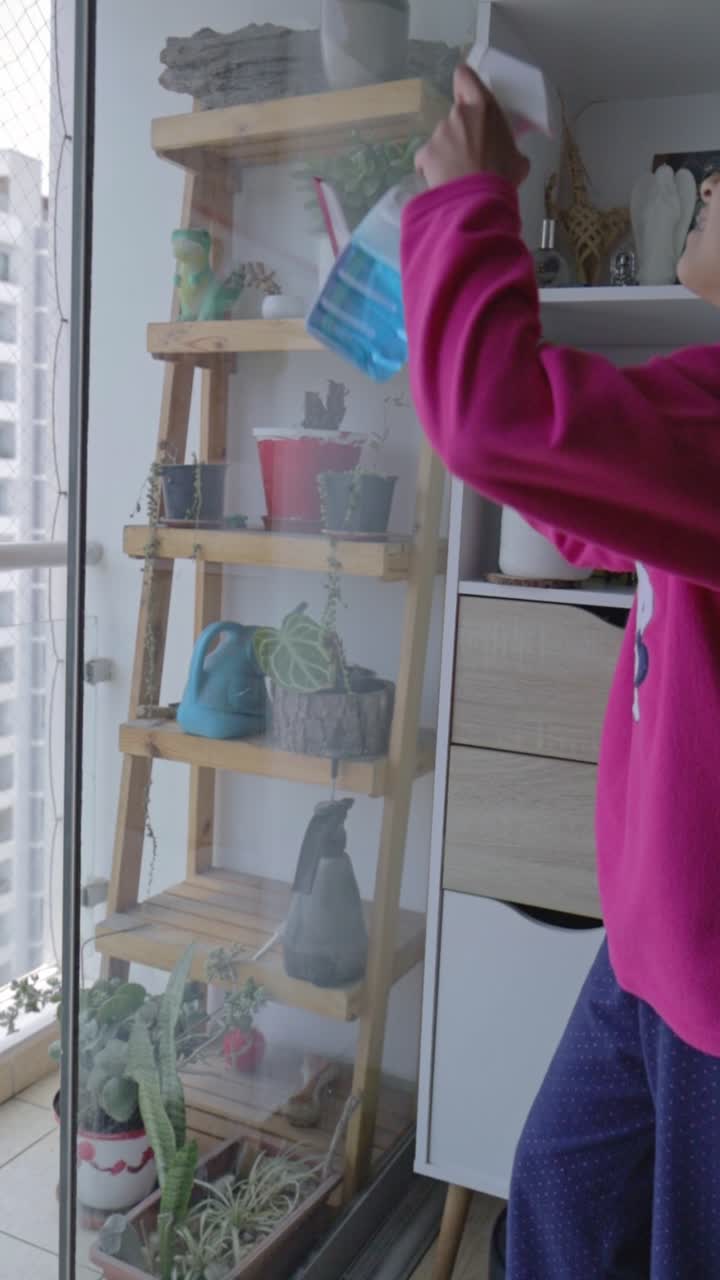 Donna che pulisce la finestra di vetro su un balcone con vista sulla città.