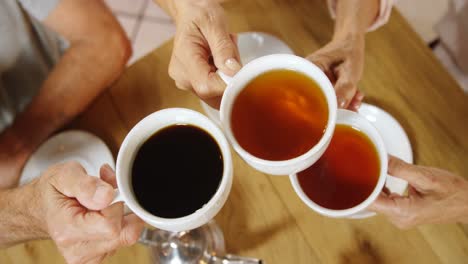 Senior-friends-toasting-black-coffee-and-tea-cups-in-cafe-4k