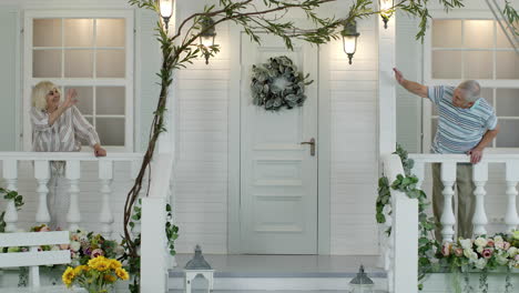 Senior-elderly-couple-waving-hands-each-to-other,-making-air-kisses-while-staying-in-porch-at-home