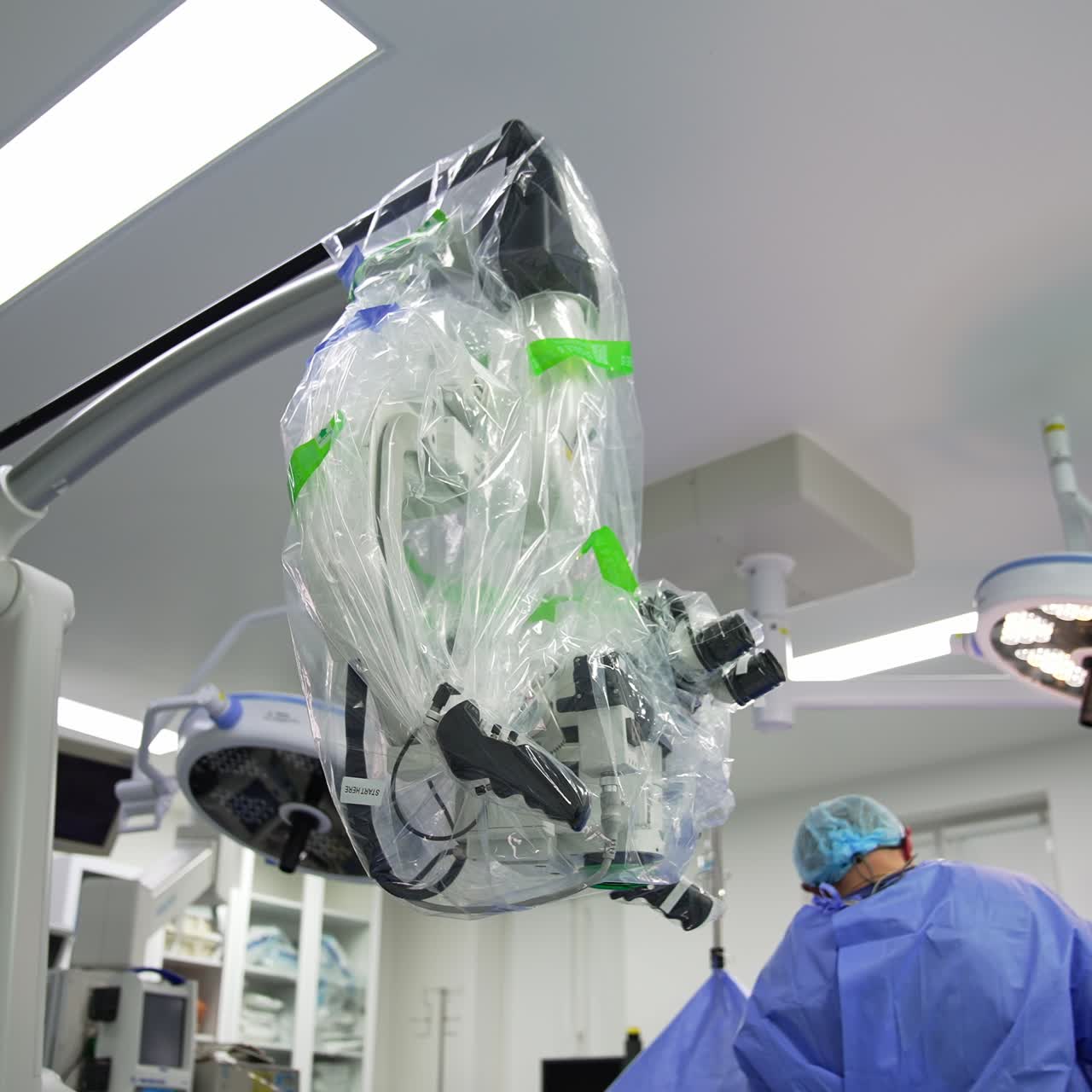 Technological advanced equipment prepared for operation. Microscope covered with plastic for sterility in surgery room. Low angle view. Doctors working in the room at backdrop
