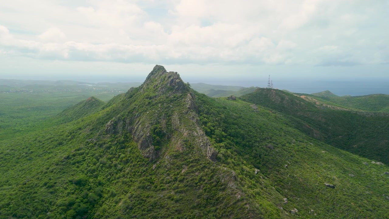 Pemandangan udara menangkap puncak berbatu Gunung Christoffel yang dikelilingi perbukitan hijau lebat dengan menara komunikasi dan laut terlihat di kejauhan di Curacao