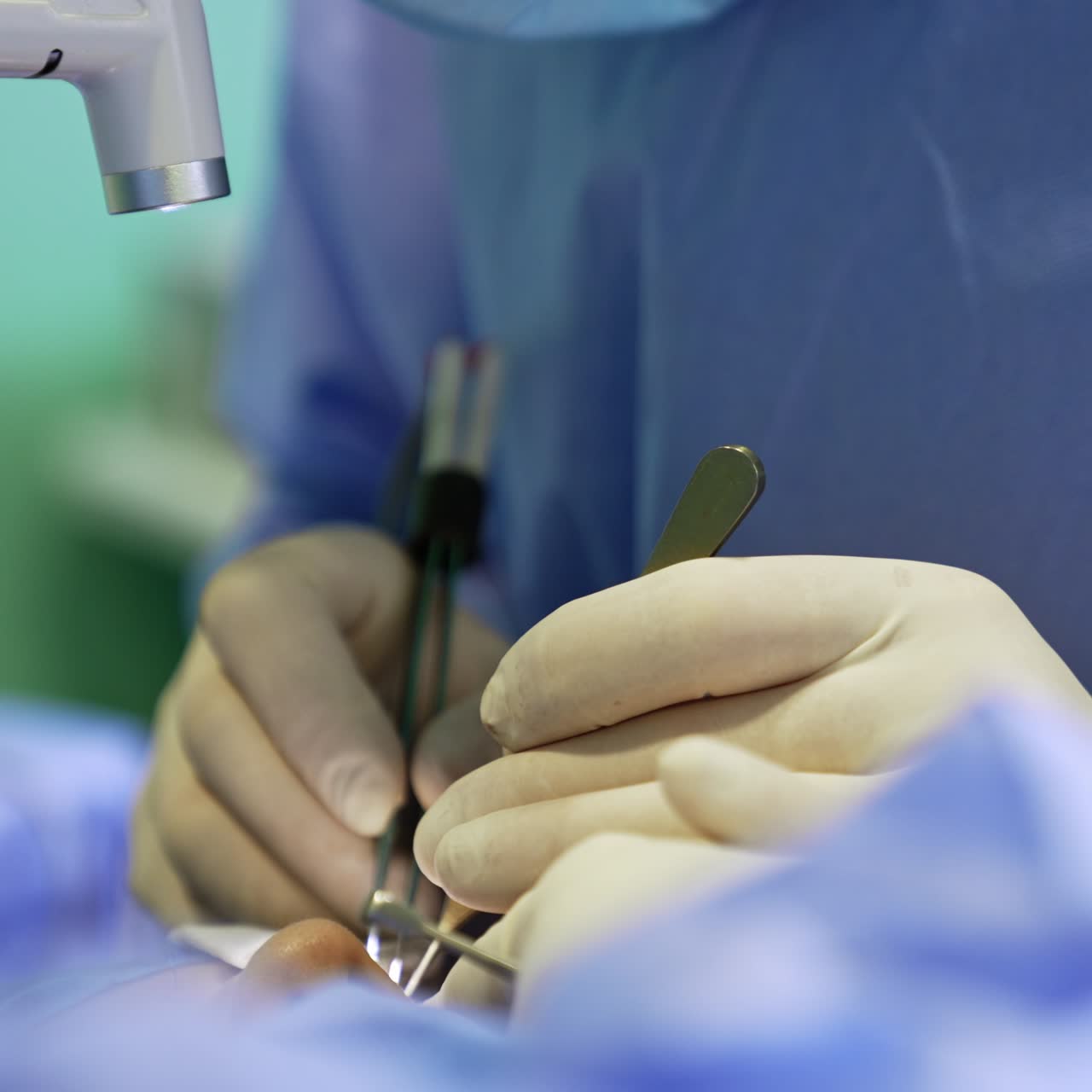 Gloved surgeon's hands hold the metal tool with one hand and take electric device with another hand. Operation on eyelid excessive skin. Close up