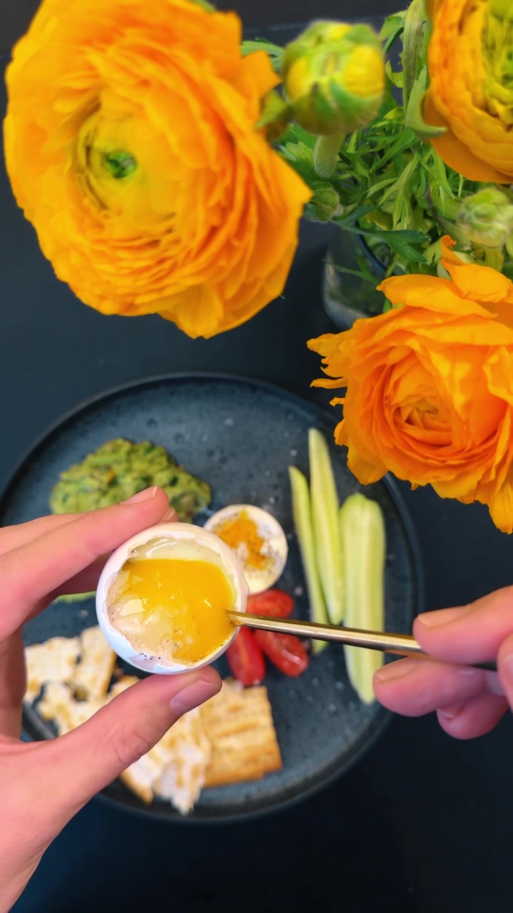 Uovo alla coque blu con tuorlo liquido e avocado. Vista dall'alto di una persona che tiene un uovo alla coque, piatto con crema di avocado, pomodoro, cetriolo e fiori d'arancio a New York