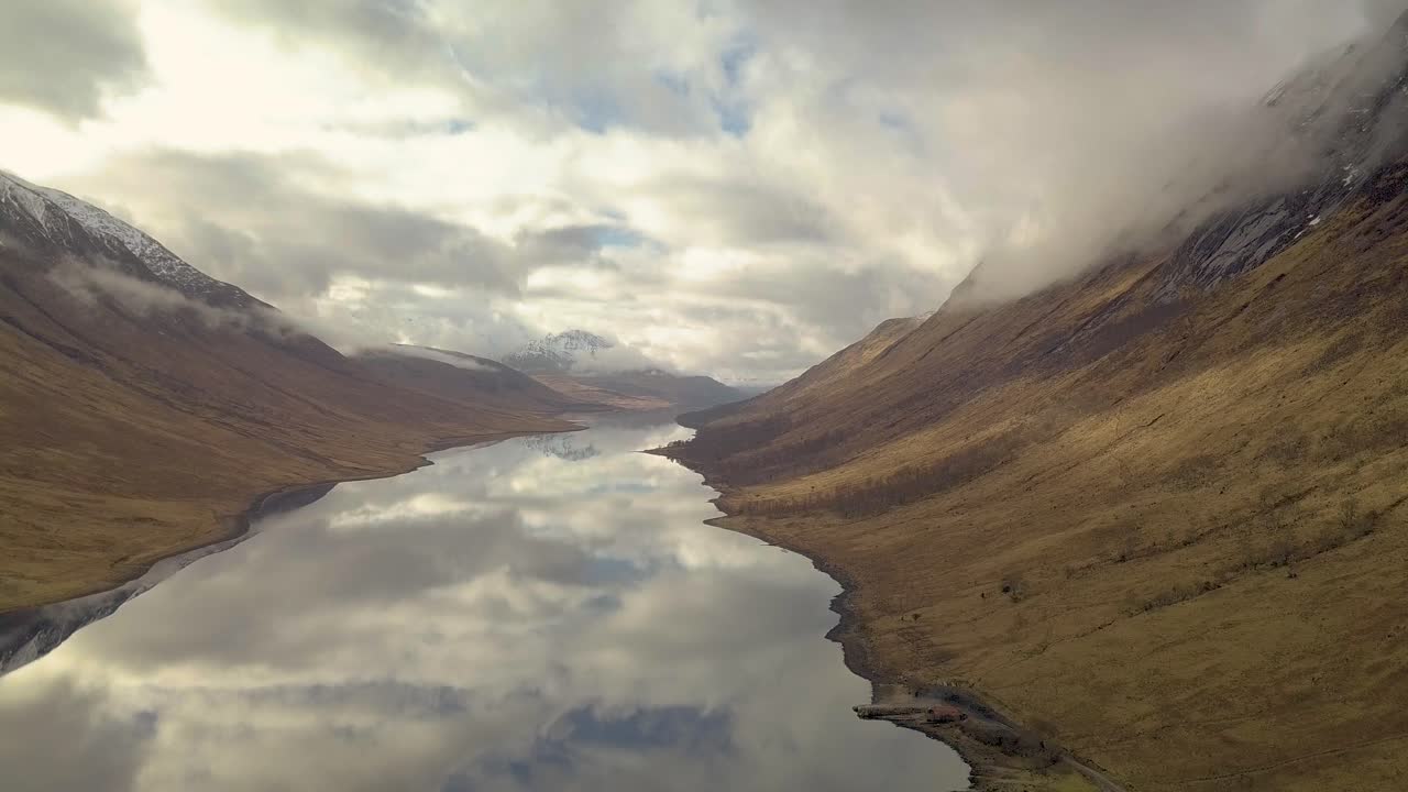 Cinematic drone shot of Scotland highlands with Glen Etive Lake during cloudy sky and reflection on water surface - wide shot