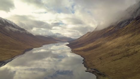 cinematic drone shot of scotland highlands with glen etive lake during cloudy sky and reflection on water surface - wide shot