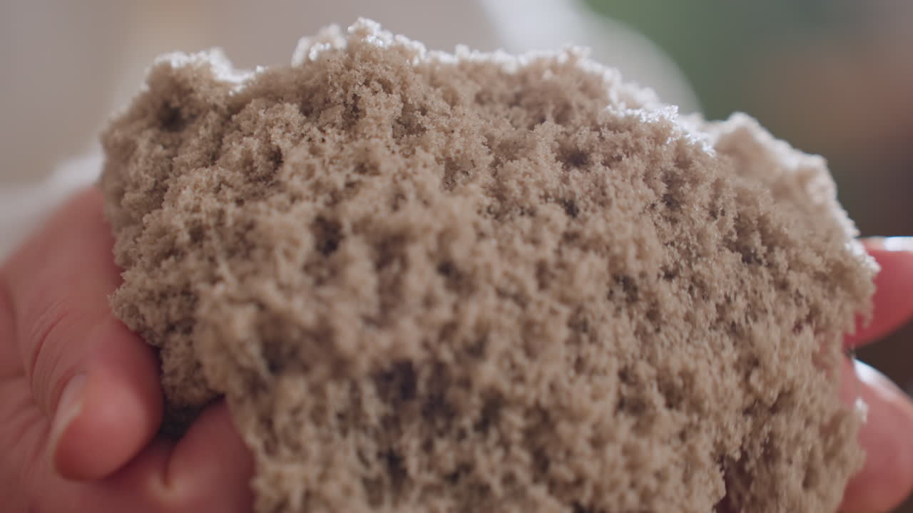 Close up of recipient of care gently lifting soft wet soil mold with both hands during calming sensory therapy session, showing textured tactile experience with blurred background details