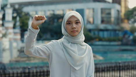 young muslim woman in hijab raising her fist in an urban setting