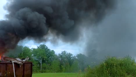 Thick-dark-smoke-billowing-from-a-burning-dumpster-full-of-garbage-on-rural-farmland