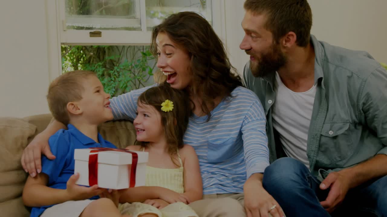 Family on couch, boy giving red-ribbon gift surprising girl laughing, tech overlays shifting around