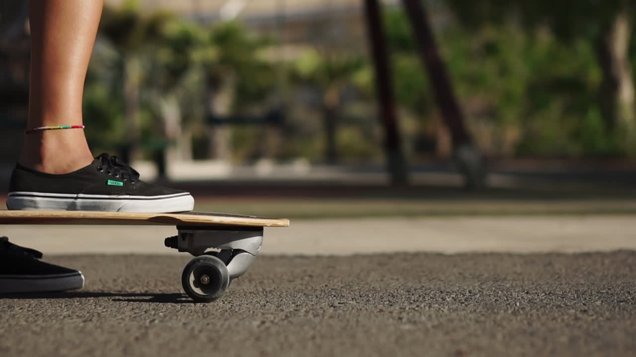 In slow motion, a beautiful young girl gracefully rides her longboard on a road by the beach and palm trees