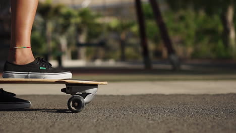 In-slow-motion,-a-beautiful-young-girl-gracefully-rides-her-longboard-on-a-road-by-the-beach-and-palm-trees