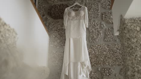 bridal gown hangs elegantly against a textured stone wall, ready for the big day