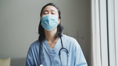 portrait of happy asian female nurse wearing face mask holding tablet in hospital, smiling to camera