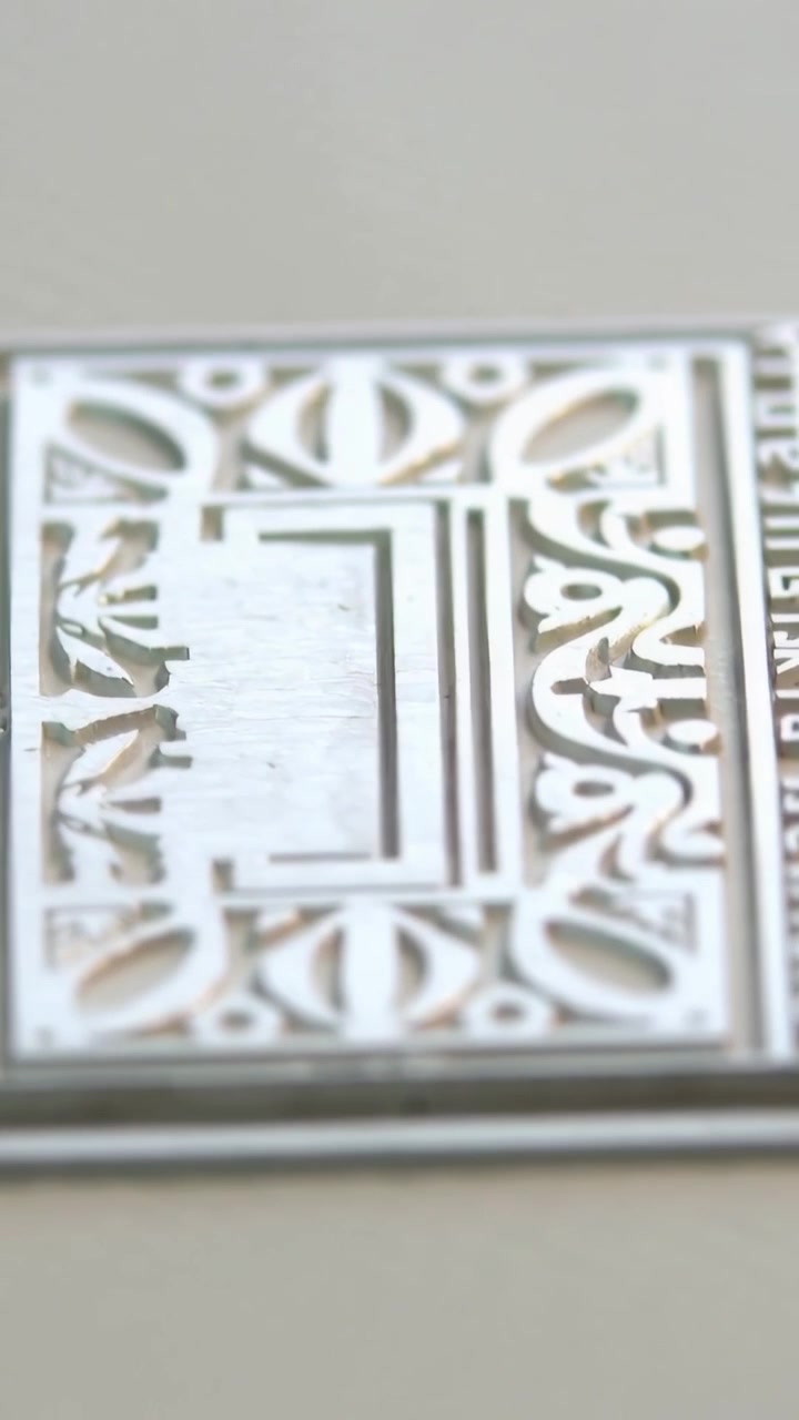 Vertical video: Shifting lens revealing ornate metal plate on ribbed card tabletop