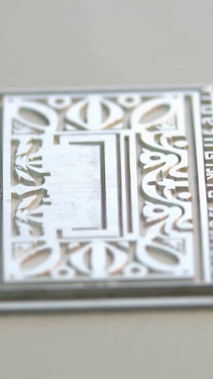 Vertical video: Shifting lens revealing ornate metal plate on ribbed card tabletop