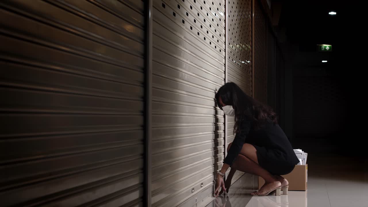 joven empresaria mujer cerrando la puerta del obturador y sentándose con un sentimiento de estrés triste en el pasillo oscuro debido al bloqueo de la segunda ola covid-19