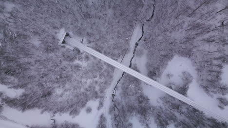 Stunning-aerial-shot-of-old-train-viaduct-seen-during-winter-in-the-middle-of-a-snowy-forest-with-a-tunnel-at-the-end-of-it