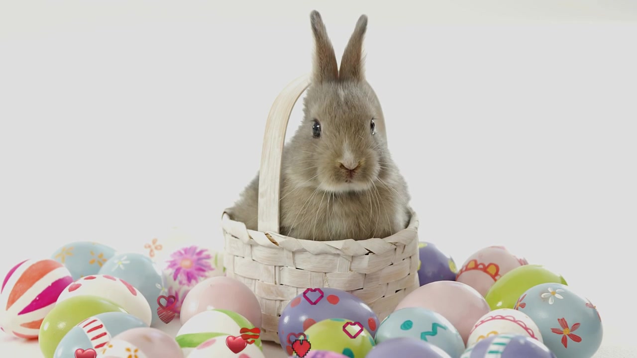 Hase sitzt in einem weißen geflochtenen Korb, Eier darunter, rot-rosa Herzen fallen von oben und erzeugen Romantik.
