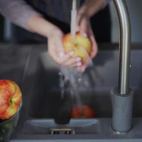 a woman washes a juicy red apple under a tap 1