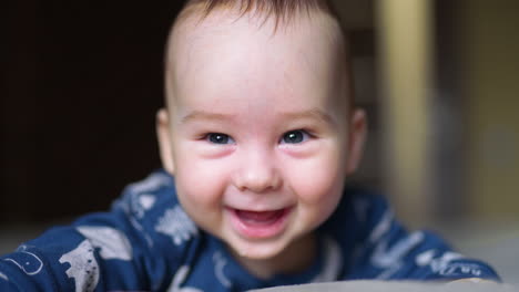 nice smiley face of a newborn baby. close up portrait of a little kid smiling cheerfully to the camera. dark backdrop in blur.