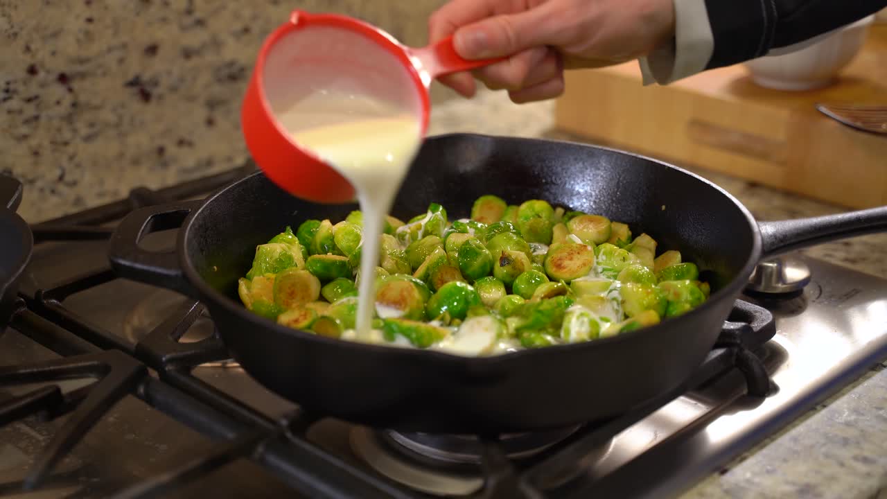 Cooking Roasted Sautéed Brussels Sprouts in a Cast Iron Pan Skillet - Pouring Cream out of Measuring Cup - Wide Shot