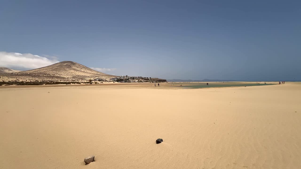 Expansive view of the vast sand flats of Sotavento Beach at low tide, with distant mountains and people walking. Fuerteventura, Canary Islands, Spain