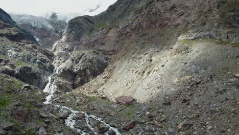 aerial flight up a massive mountain formation with wild waterfall and river, breathtaking drone shot over swiss alps in saas-fee