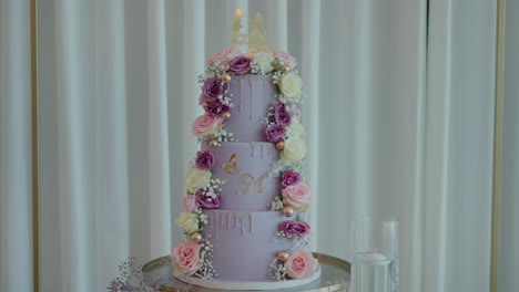 three tiered wedding cake decorated with pastel roses and a gold monogram, set against white drapes