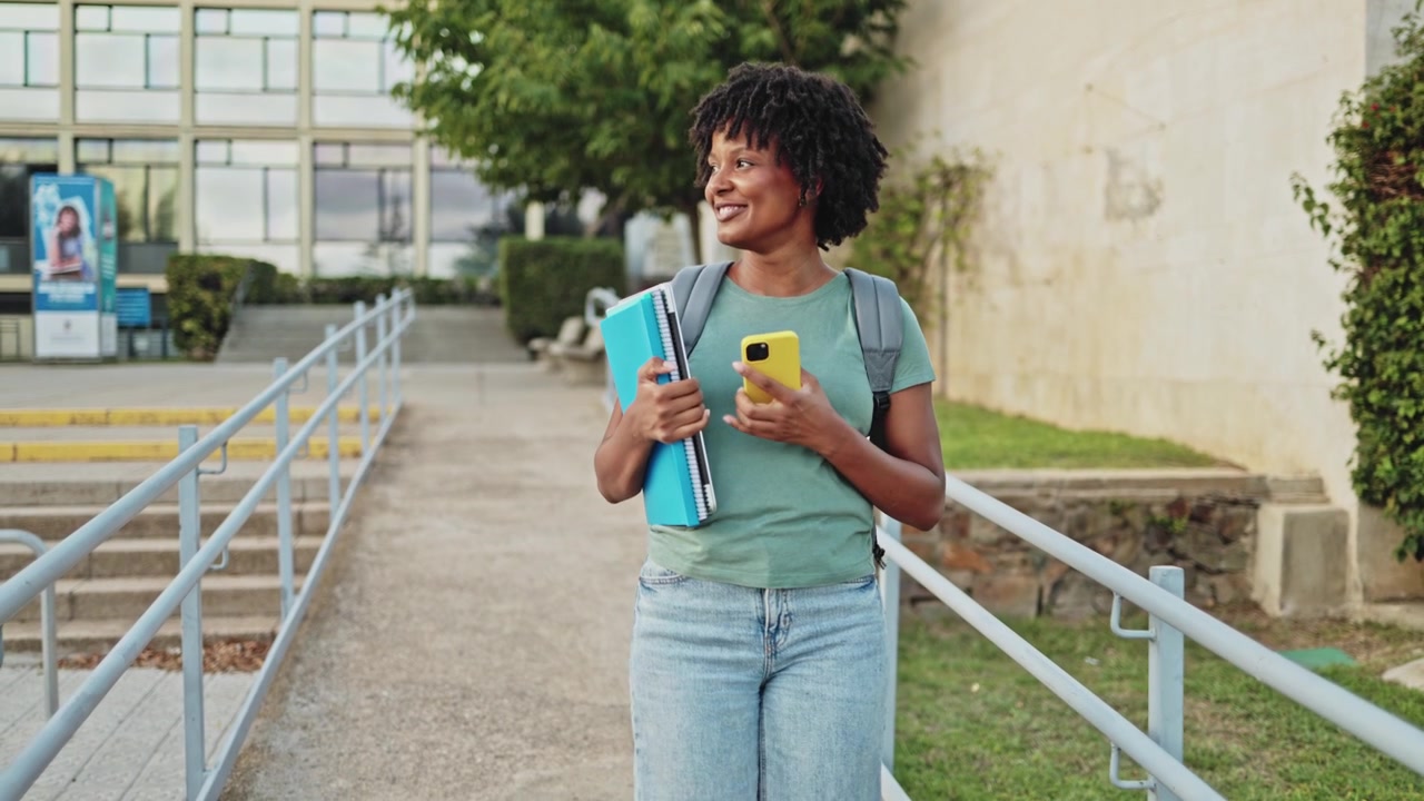 Happy African American Student Walking on Campus Using Smartphone
