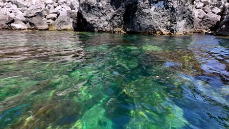 Clear-turquoise-waters-gently-lap-against-the-rocky-coastline-of-Sudak-Bay-in-Crimea,-Russia,-showcasing-the-breathtaking-beauty-of-the-Black-Sea