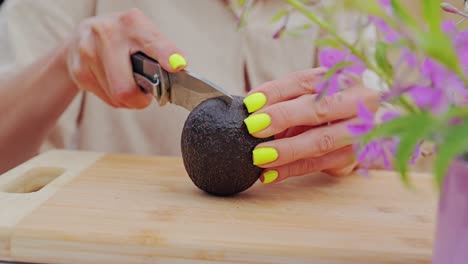 woman’s bright nails slice avocado skin slowly at rustic campsite table