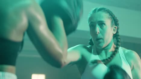 medium shot of a strong caucasian sportswoman training with coach, wearing boxing gloves and punching boxing paws