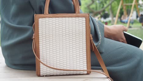 woman with a white woven handbag in a park