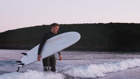 man wearing wetsuit carrying surfboard as he walks out of sea