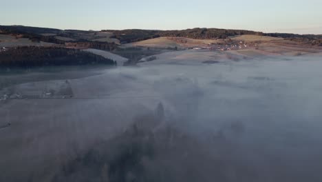 An-aerial-view-of-the-fog-shrouded-Sumava-landscape-with-hills,-forests-and-fields,-a-peaceful-and-natural-scene