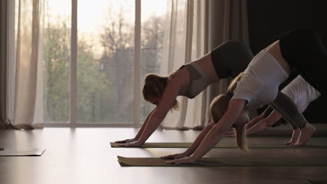 En-Cámara-Lenta,-Un-Entrenamiento-Conjunto-De-Pilates-Femenino-Con-Un-Instructor-Muestra-A-Mujeres-Delgadas-Y-Regordetas-En-El-Gimnasio-Por-La-Mañana-Bajo-El-Sol.-El-Resplandor-Del-Sol-En-El-Suelo