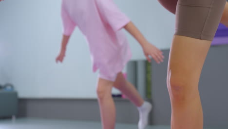 primer plano de niños en un gimnasio practicando el equilibrio en una pierna, con una joven de color rosa centrándose atentamente en mantener su postura en medio de una sesión de fitness