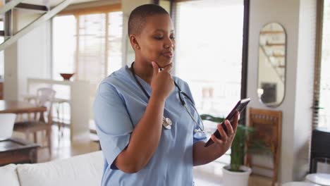 African-american-female-doctor-having-video-call-consultation-using-tablet-looking-to-camera-smiling